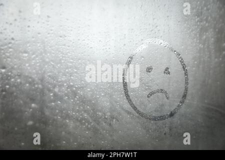 Trauriges Gesicht auf nebligem Fenster, Platz für Text. Regenwetter Stockfoto