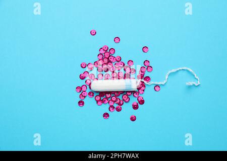 Tampon und pinkfarbene Pailletten auf hellblauem Hintergrund, flach liegend. Menstruationshygieneartikel Stockfoto