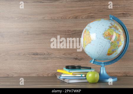 Globus, Bücher, Lupe und Apfel auf Holztisch, Platz für Text. Geografie-Lektion Stockfoto