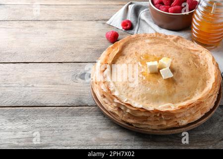 Ein Haufen köstlicher Crepes, serviert mit Butter, Honig und Himbeeren auf einem Holztisch. Platz für Text Stockfoto