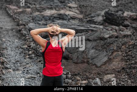 Müder Läufer erschöpft auf dem Bergweg, der eine Pause mit Rückenschmerzen auf dem vulkanischen Felsweg mit schwarzer Lava im Sommer Hawaii macht Stockfoto