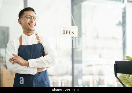Porträt eines wunderschönen Asiaten, der ein kleines Unternehmen leitet und ein lächelndes Gesicht zeigt, ein Coffee Shop-Besitzer eröffnet einen Laden, um Kunden im neuen zu begrüßen Stockfoto