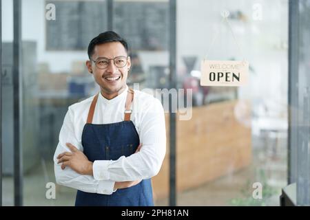Porträt eines wunderschönen Asiaten, der ein kleines Unternehmen leitet und ein lächelndes Gesicht zeigt, ein Coffee Shop-Besitzer eröffnet einen Laden, um Kunden im neuen zu begrüßen Stockfoto
