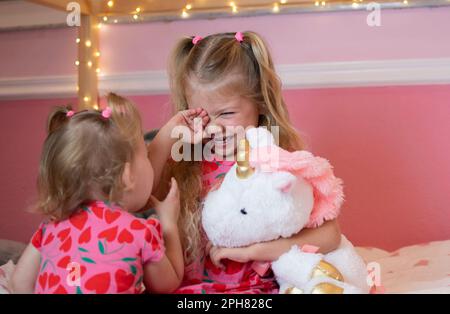 Weinendes kleines Mädchen mit ihrer Schwester. Geschwisterliebe und Beziehungskonzept. Ein Kleinkind tröstet ihre weinende Schwester Stockfoto