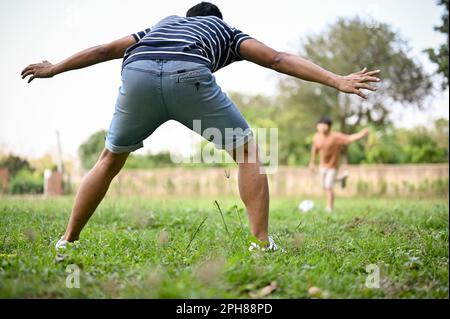 Fröhlicher und glücklicher asiatischer Vater, der mit seinem Sohn im Garten Fußball spielt. Outdoor-Aktivitäten und ein glückliches Familienkonzept Stockfoto