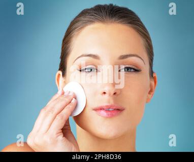 Hier ist kein Öl. Studio-Porträt einer wunderschönen jungen Frau, die sich mit einem Baumwolltupfer vor blauem Hintergrund das Gesicht abwischte. Stockfoto
