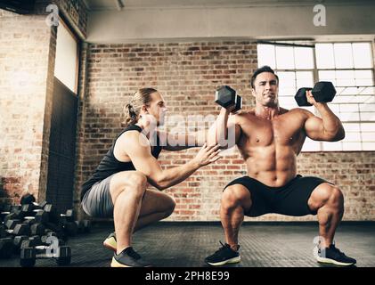 Achte darauf, dass dein Rücken immer gerade ist. Zwei fitte und entschlossene junge Männer, die sich gegenseitig beim Gewichtheben in einem Fitnessstudio helfen. Stockfoto