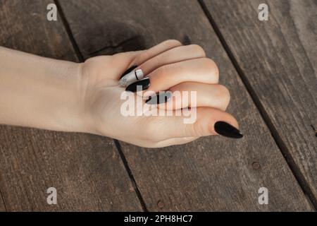 Verlängerte Nägel mit Maniküre in schwarz-weiß auf Holzhintergrund, weibliche Maniküre Stockfoto