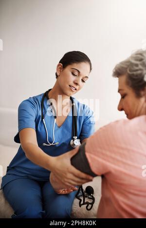 Ich mache eine Routineuntersuchung. Eine attraktive junge Krankenschwester, die den Blutdruck eines Seniorenpatienten prüft. Stockfoto