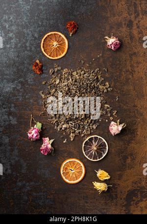 Grüner, trockener Tee, Blumentee und trockene Orangenchips auf braunem Hintergrund, Draufsicht. Verschiedene Teesorten und trockene Zitrusscheiben auf dunklem Hintergrund. Stockfoto
