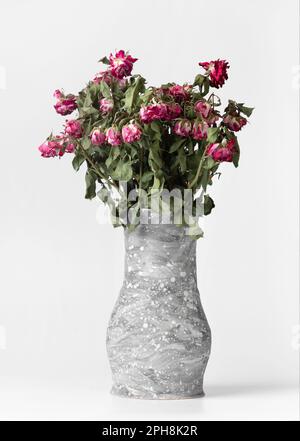 Handgemachte Vase mit einem Strauß trockener Blumen isoliert. Trockene Rosen in einer Lehmvase auf weißem Hintergrund. Graue Vase mit einem Strauß getrockneter Blumen. Stockfoto