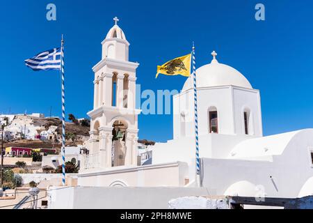 Kirche und Glockenturm im typisch griechischen Stil in Santorin mit griechischer Flagge und gelbem Doppelkopfadler Stockfoto