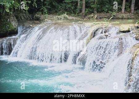 Die idyllischen Cambugahay Wasserfälle in Siquijor auf den Philippinen fließen in ein natürliches Wasserbecken, umgeben von dem lichtdurchfluteten Regenwald. Stockfoto