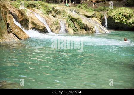 Die idyllischen Cambugahay Wasserfälle in Siquijor auf den Philippinen fließen in ein natürliches Wasserbecken, umgeben von dem lichtdurchfluteten Regenwald. Stockfoto