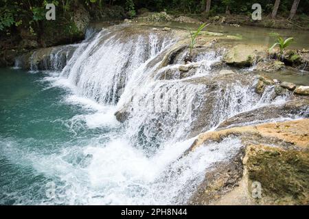 Die idyllischen Cambugahay Wasserfälle in Siquijor auf den Philippinen fließen in ein natürliches Wasserbecken, umgeben von dem lichtdurchfluteten Regenwald. Stockfoto