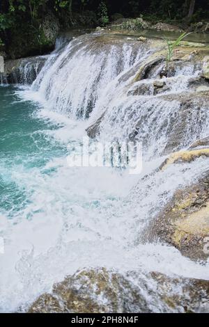 Die idyllischen Cambugahay Wasserfälle in Siquijor auf den Philippinen fließen in ein natürliches Wasserbecken, umgeben von dem lichtdurchfluteten Regenwald. Stockfoto