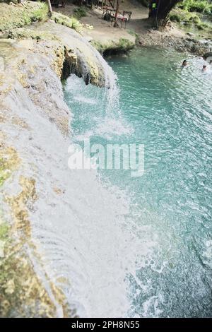 Die idyllischen Cambugahay Wasserfälle in Siquijor auf den Philippinen fließen in ein natürliches Wasserbecken, umgeben von dem lichtdurchfluteten Regenwald. Stockfoto