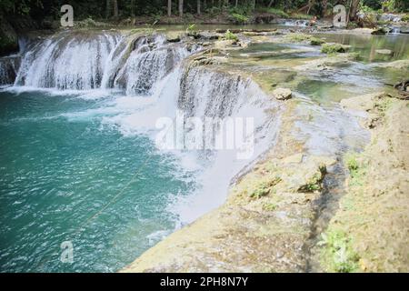 Die idyllischen Cambugahay Wasserfälle in Siquijor auf den Philippinen fließen in ein natürliches Wasserbecken, umgeben von dem lichtdurchfluteten Regenwald. Stockfoto