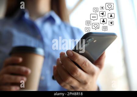 Verschiedene virtuelle Ikonen und junge Frau, die ihr Smartphone drinnen benutzt, Nahaufnahme. SMM-Konzept (Social Media Marketing) Stockfoto