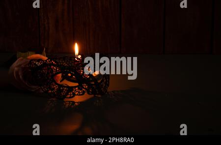 Kerzenflamme und neben einer Rose und Spitze Gesichtsmaske für Karneval im Dunkeln Nahaufnahme Stockfoto