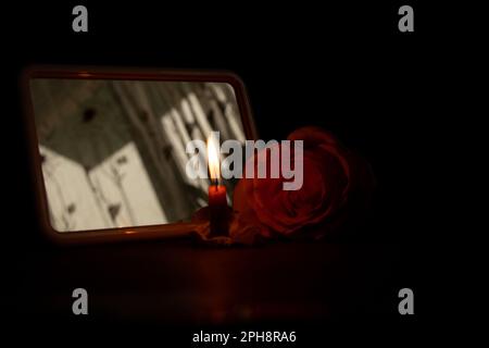 Eine Kerzenflamme und neben einer Rose in der dunklen Nahaufnahme Stockfoto