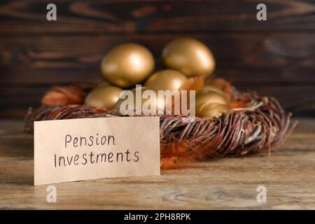 Viele goldene Eier und Karte mit Phrase Pension Investments auf Holztisch, Platz für Text Stockfoto