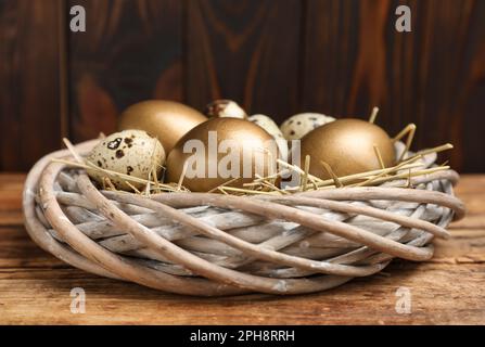 Goldene und Wachteleier im Nest auf einem Holztisch, Nahaufnahme Stockfoto