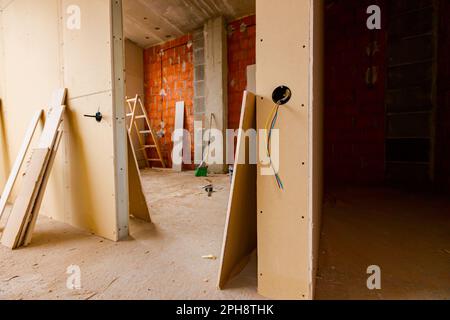 Eine freiliegende Steckdose mit entfernter oberer Abdeckung für die Installation der Verkabelung an der Trennwand aus Gipskartonplatten, das Gebäude befindet sich unter dem Bau Stockfoto