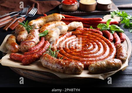 Verschiedene köstliche Würstchen mit Kräutern auf einem schwarzen Holztisch. Auswahl an Biersnacks Stockfoto