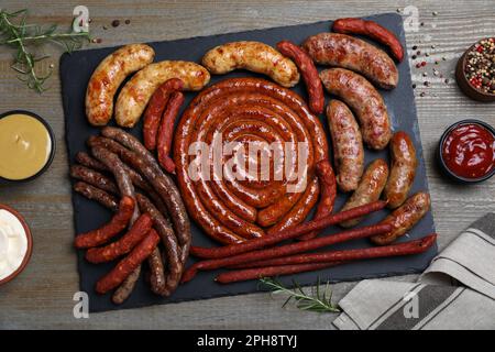 Verschiedene leckere Würstchen und Saucen auf Holztisch, flach liegend. Auswahl an Biersnacks Stockfoto