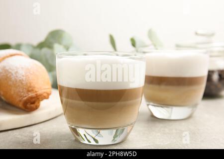 Köstlicher Latte Macchiato und Croissant auf hellgrauem Tisch Stockfoto
