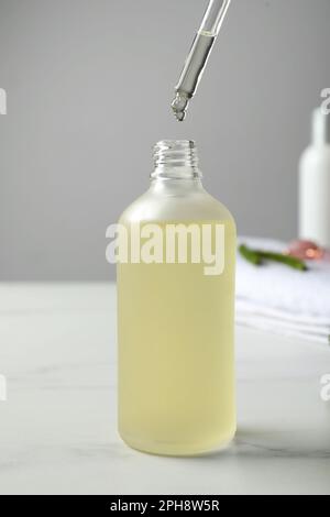 Tropfen von hydrophilem Öl in die Flasche auf dem weißen Tisch, Nahaufnahme Stockfoto