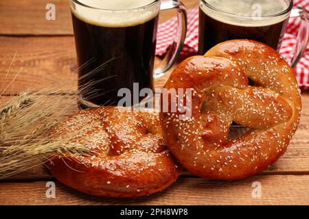 Leckere frisch gebackene Brezeln, Stacheln und Becher Bier auf Holztisch, Nahaufnahme Stockfoto