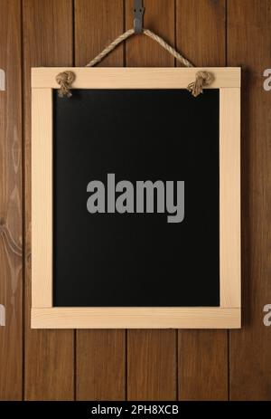 Saubere kleine schwarze Tafel, die an der Holzwand hängt Stockfoto