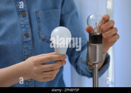 Frau wechselt Glühlampe gegen Leuchtstofflampe zu Hause, Nahaufnahme. Energiesparkonzept Stockfoto