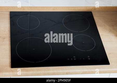 Moderne Küche mit schwarzem Induktionskochfeld oder Elektroherd mit Keramikoberfläche und Holzarbeitsfläche Stockfoto