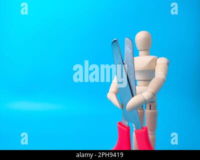 Schaufensterpuppe aus Holz mit roter Schere auf blauem Hintergrund und Kopierbereich. Stockfoto