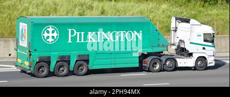 Scania White lkw-Triebwerk und Fahrer St Helens Pilkington Markenname und Logo Seitenansicht des grünen Anhängers, der auf der britischen Autobahn M25 fährt Stockfoto