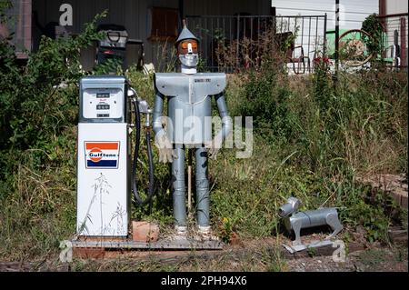 Eine metallische Roboterfigur steht neben einer Zapfsäule in einem grasbedeckten Bereich Stockfoto