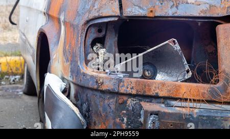 Verbrannte Karosserie. Brandstiftung, Kurzschluss. Das Skelett eines verbrannten Autos. Vorderansicht eines verbrannten und verlassenen rostigen Lieferwagens und eines kaputten Scheinwerfers Stockfoto