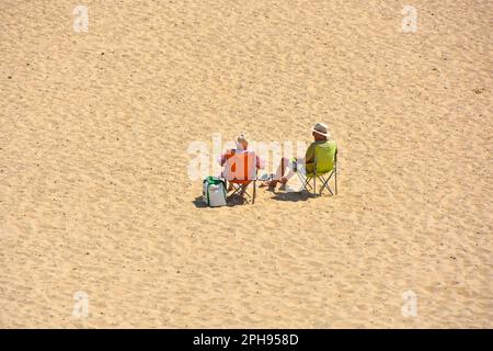 Wir blickten auf ein älteres Paar, das allein in Liegen auf einer scheinbar abgelegenen, leeren Weite von sauberem Sand am Meer in Sonnenhütten saß, heißes, sonniges Wochenende in Großbritannien Stockfoto