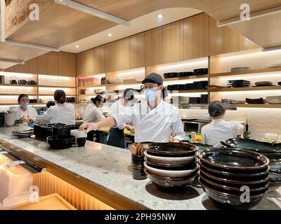 Unbekannte Menschen in Masken und Handschuhen bereiten japanisches chinesisches Essen in einem Sushi-Restaurant zu, Männer und Frauen in weißen Kleidern in Schürzen, ordentlich gekleidet, steril gekleidet, Kanada Vancouver 2023 Stockfoto