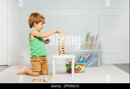 Ein Junge baute Jenga-Turm aus Holzblöcken auf dem Teppich in einem Zimmer Stockfoto