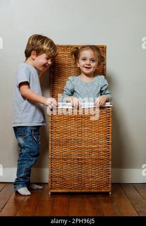 Junge und Mädchen verstecken sich im Wäschekasten aus Holz Stockfoto