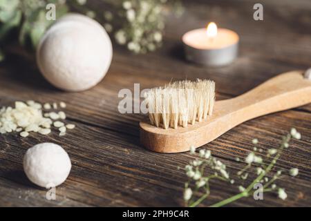 Spa-Zusammensetzung mit Bürste, Kerze und getrockneten Blumen auf Holzfläche. Stockfoto