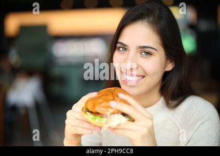 Eine glückliche Frau, bereit, in einem Restaurant Burger zu essen und vor die Kamera zu schauen Stockfoto