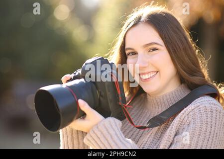 Ein glücklicher Fotograf mit dslr-Kamera sieht Sie in einem Park an Stockfoto