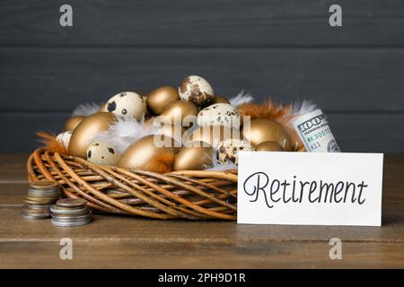 Viele goldene und Wachteleier im Nest, Geld in der Nähe der Karte mit Wort Ruhestand auf einem Holztisch. Pensionskonzept Stockfoto