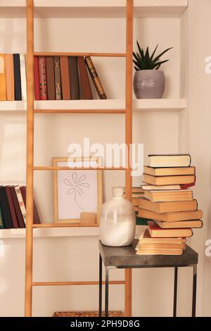 Stapel verschiedener Bücher und Vasen auf einem Tisch neben Bücherregalen in der Hausbibliothek Stockfoto