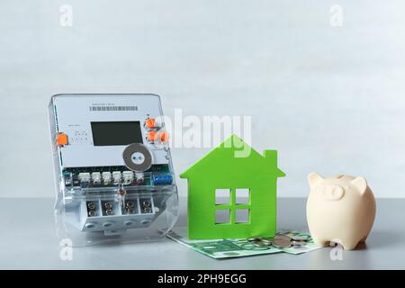 Stromzähler, Sparschwein und Euro-Banknoten auf grauem Tisch Stockfoto